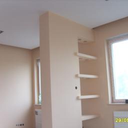 Grand-Tech - Wykończone wnętrze w jasnych odcieniach beżu, z ścianką działową z półkami i wbudowanym oświetleniem punktowym, widok na okno z parapetem.